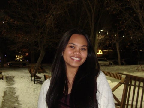 Smiling woman with long dark hair wearing a white cardigan and maroon top at an outdoor snowy venue at night