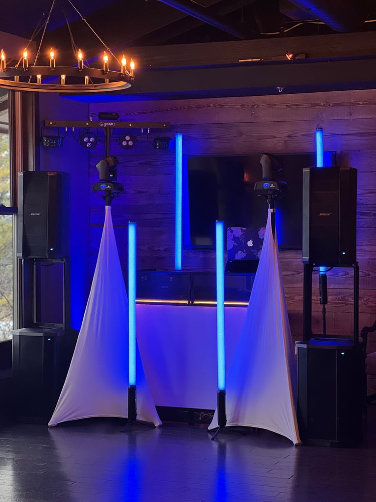 Modern DJ booth with neon blue lighting, draped white fabric, vertical light panels, and wooden wall backdrop in an event venue