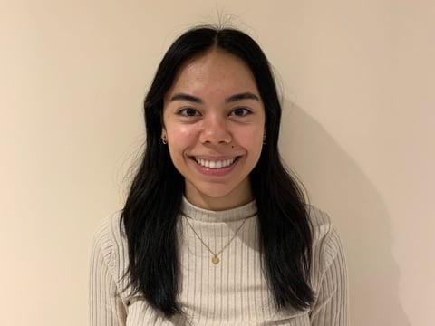 Portrait of a smiling young woman with long black hair wearing a beige ribbed sweater