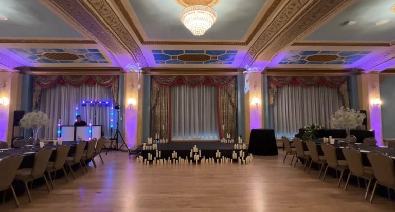Elegant ballroom with purple ambient lighting, ornate ceiling, wooden stage setup, and rows of seating arranged for an event
